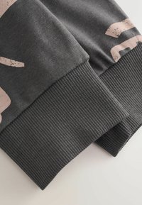 Cuff di felpa grigia scura con texture a coste e stampa astratta beige chiaro. Presenta una vista ravvicinata che mostra dettagli di cucitura e tessuto.