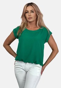 Zielony krótki rękaw top z gładkiego materiału z okrągłym dekoltem, zestawiony z białymi dopasowanymi spodniami. Prosty design bez widocznych wzorów.