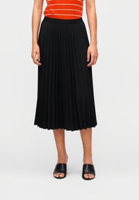 Μαύρη πλισέ midi φούστα με υφή υφάσματος, ελαστική μέση και ρέον σχέδιο. Φορεμένη με μαύρα σανδάλια slide.