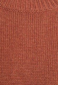Tissu de pull en tricot dans une riche couleur orange brûlée, avec une texture côtelée et un col haut. Fil robuste avec un motif uniforme.