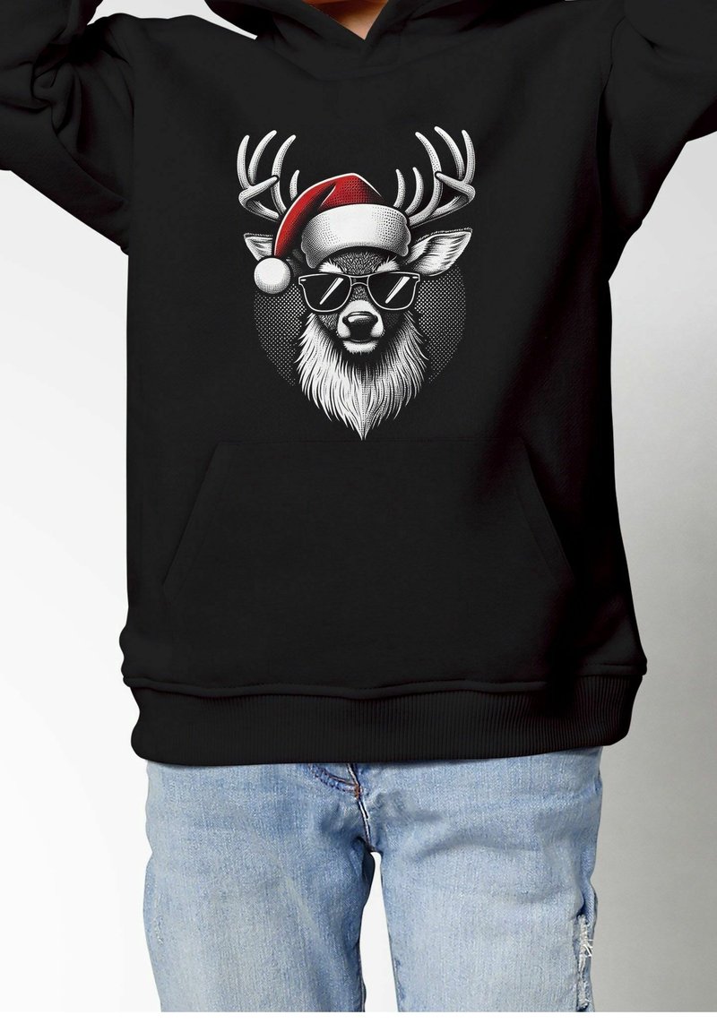 Tête de renne stylisée portant des lunettes de soleil et un chapeau de Père Noël rouge, imprimée sur un sweat à capuche noir porté avec un jean bleu clair.