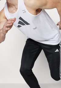 Bílý sportovní tíLko s černými detaily loga, spojené s černými těsnými kalhotami s bílými pruhy a logem, které ukazují elegantní design.
