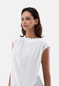 Blusa bianca senza maniche con scollatura plissettata, dalla texture morbida e vestibilità rilassata. Il tessuto cade naturalmente, offrendo una silhouette pulita.