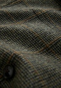 Close-up of textured brown and green tweed fabric with a subtle check pattern and a dark button.