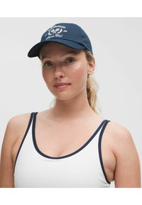 Námořnická modrá bavlněná čepice s vyšitým textem a designem. Bílé akcenty a zakřivený kšilt. Nosí se s bílým tílkem bez rukávů s námořnickým lemov�áním.