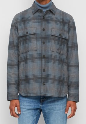 Chaqueta de cuadros en tonos de azul y gris, de mezcla de lana texturizada, con dos bolsillos en el pecho y un cuello, llevada sobre un cuello de tortuga azul.