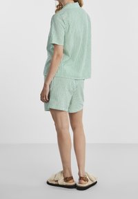 Zielona i biała w paski koszulka z krótkim rękawem oraz dopasowane szorty, wykonane z lekkiego materiału. Uzupełnione kremowymi, puszystymi sandałami.
