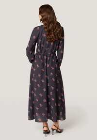 Lang, donker bloemig jurkje met lange mouwen en een elastische taille. Heeft een patroon van kleine roze bloemen en een luchtige, lichte stof.