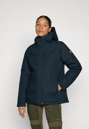 Navyblauwe gevoerde jas met een hoge kraag en een afneembare capuchon. Voorzien van drukknoopsluitingen, zijzakken en een logo-opnieuw op de schouder.