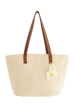 Beige vævet tote taske med brune skulderremme og to hvide kunstige blomster som pynt.