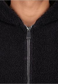 Svart fleecetröja med dragkedja, med en texturerad och mjuk yta. Dragkedjan är metallisk och kontrasterar med tyget.