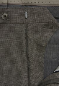 Tissu texturé gris avec un motif subtil, doté d'une fermeture à bouton, d'une fermeture éclair et de détails de poche latérale. Doublure intérieure lisse de contraste.
