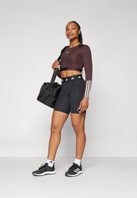 Smeđi dugi crop top s bijelim prugama, crne visoke kratke hlače, crne tenisice i crna torba.