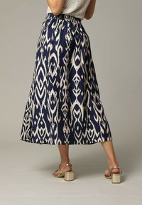 Jupe maxi en bleu marine et crème, avec un design fluide, une taille élastique et un motif ikat abstrait. Associée à des sandales à talons blocs beiges.