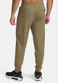 Brune atletiske joggingbukser med elastisk talje, sidelommer og en baglommer. Båret med sorte sneakers med en hvid sål.