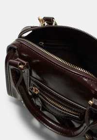 Ciemnobrązowa skórzana torebka z złotymi zamkami i elementami, częściowo otwarta, pokazująca wewnętrzną kieszeń na zamek oraz usztywniony uchwyt.