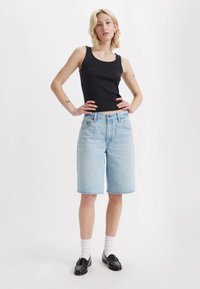 Calções de ganga azul claro com um corte descontraído e bainhas dobradas, combinados com uma t-shirt preta de malha, meias brancas e mocassins pretos.