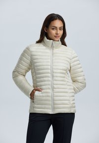 Lyse beige puffjakke med høj krave, vandret quilting, lynlåslukning foran og sidelommer. Glat, glansfuld overflade.