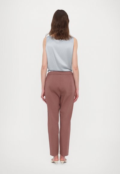 Jasnoniebieska bezrękawnik o gładkiej fakturze, zestawiony z różowo-brązowymi spodniami o tapered cut, z bezszwowym paskiem w talii i długością sięgającą kostek.