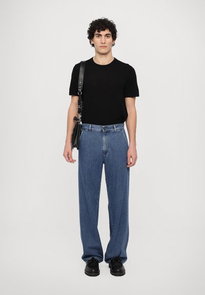 Black short-sleeve t-shirt, light blue loose-fitting denim jeans, black leather crossbody bag, and black lace-up shoes. Plain background.