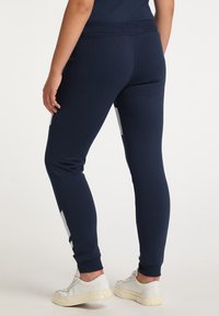 Donkerblauwe sweatpants met een fitted ontwerp, gemaakt van zacht materiaal. Voorzien van grijze zijpanelen en geribde boorden, gecombineerd met witte sneakers.