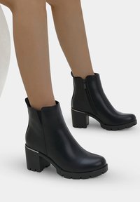 Botas negras hasta el tobillo hechas de cuero suave con un tacón de bloque, cierre de cremallera lateral y suela texturizada para agarre.