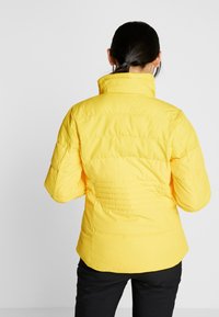Gelbe gepolsterte Jacke mit hohem Kragen und gesticktem Muster, schlanker Silhouette und langen Ärmeln, aus glattem Stoff gefertigt.