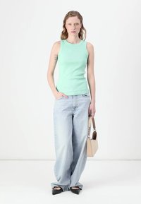 Mintgrønn tank topp, lyseblå vide jeans, svarte spisse flats, og en beige håndveske med "HUGO" trykk. Enkel design, uformell stil.