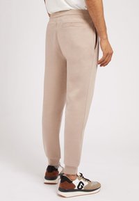 Pantalones de chándal beige con un corte ajustado, cintura elástica y bolsillos laterales. Combinados con zapatillas multicolores que presentan acentos en negro y marrón.