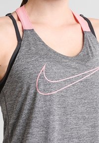 Gray athletic tank top featuring a scoop neckline, black and pink straps, and a pink Nike swoosh logo on the front. Polyester blend fabric.