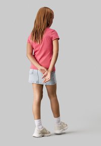 Camiseta de manga corta rosa, falda de mezclilla clara por encima de la rodilla, calcetines blancos y zapatillas deportivas de color claro. El cabello es largo y liso.