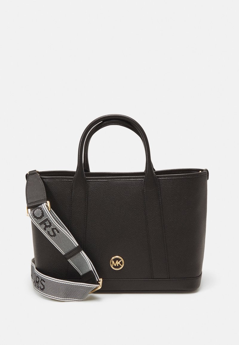 Sac fourre-tout en cuir texturé noir avec double poignées et une sangle amovible, arborant le logo "MK" et une lettrage en gras à rayures.