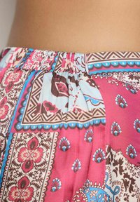 Primo piano di una gonna colorata con vita elastica, caratterizzata da motivi floreali e geometrici in tonalità di rosso, blu, marrone e crema, appoggiata su pelle nuda.