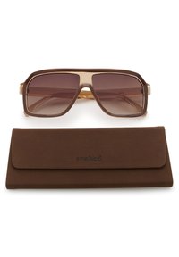 Lunettes de soleil carrées marron oversize avec verres dégradés, posées sur un étui souple assorti marron embossé du mot « soaked ».