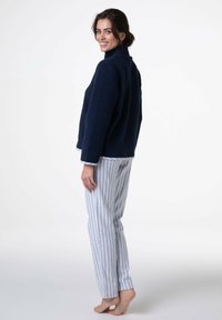 Giacca in pile blu navy con collo alto, tasche laterali e rifiniture bianche, abbinata a pantaloni del pigiama leggeri a righe. Tessitura liscia e vestibilità comoda.
