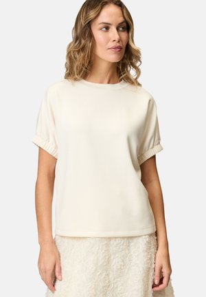 Crème-kleurige top met korte mouwen en gathering bij de mouwen, ronde halslijn en een gladde textuur. Gecombineerd met een lichtgekleurde rock met textuur.