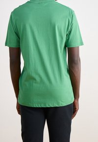 Camiseta de algodón verde con mangas cortas y cuello redondo. Textura suave, diseño básico, sin patrones ni gráficos visibles.