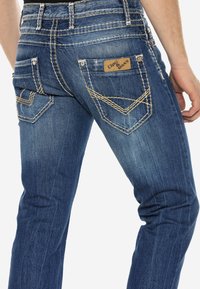 Blauwe denim jeans met een vervaagde afwerking, contrasterende stiksels en decoratieve achterzakken. Beschikt over een merklabel op de tailleband.
