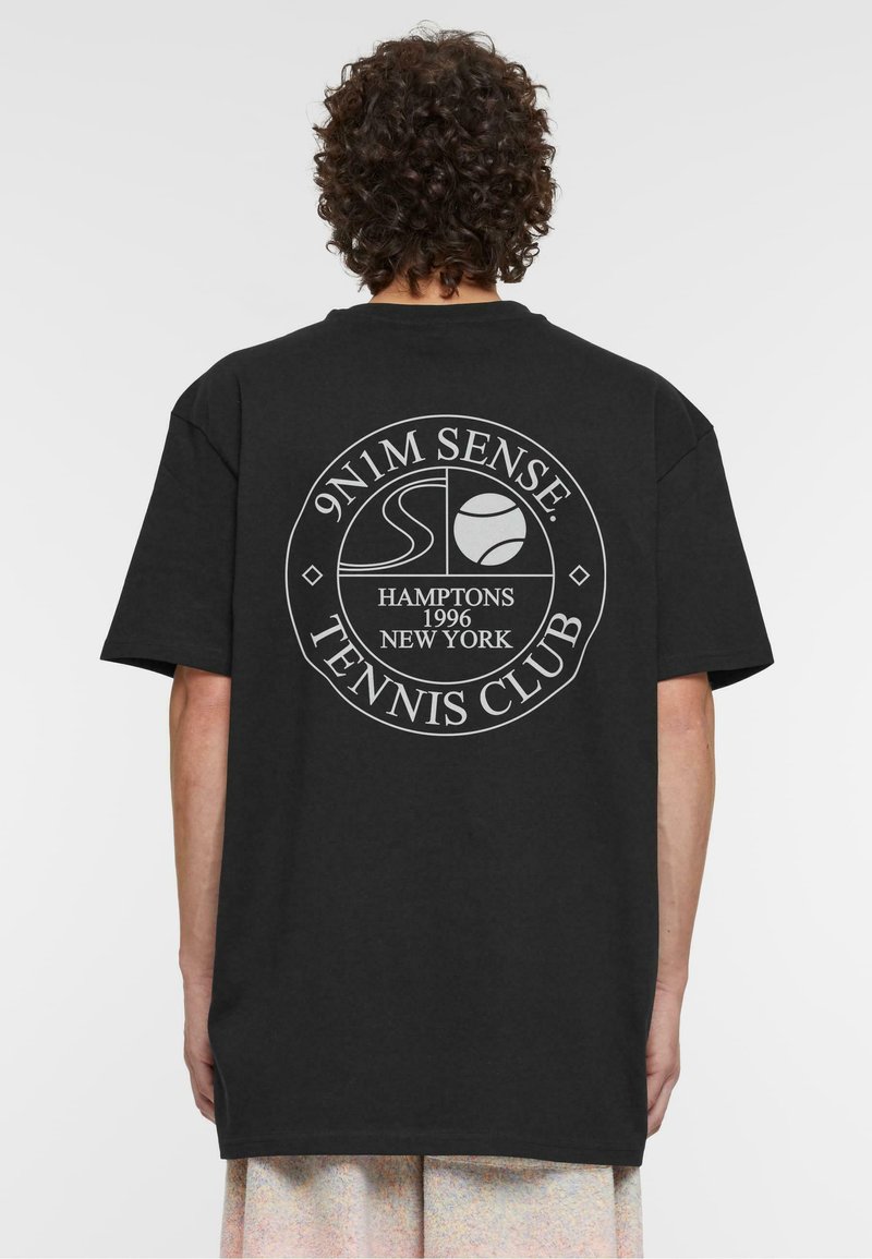 Melna T-krekls ar īsām piedurknēm, uz muguras ar apaļu balti izdrukātu logotipu. Uzraksts ietver "9N1M SENSE", "HAMPTONS" un "TENNIS CLUB".