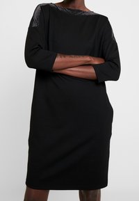 Robe noire à manches trois quarts, en matériau doux, coupe décontractée, avec un accent scintillant au niveau du col. Design uni, longueur genou.