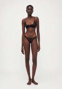 Black lace lingerie set featuring a bralette with thin straps and matching thong, showcasing floral patterns and sheer texture.