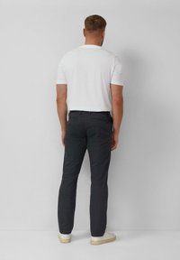 Męskie ciemnoszare spodnie z teksturowanym wzorem, o wąskim kroju, z zapinanymi na guziki tylnymi kieszeniami, w połączeniu z białą koszulą z krótkim rękawem i białymi tenisówkami.