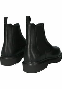 Botas de cuero negro hasta el tobillo con paneles laterales elásticos, tiradores y suelas de goma gruesas que presentan una textura robusta y una ligera elevación del tacón.