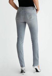 Jeans in denim grigio slim con tasche posteriori decorate con cuciture e abbellimenti. Indossati con scarpe con tacco alto argentate.