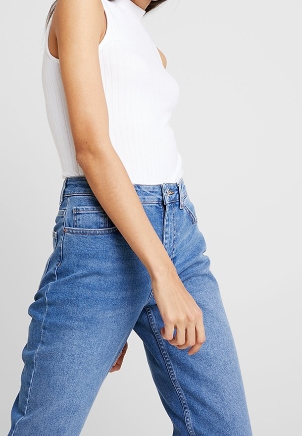 Top sin mangas blanco acanalado combinado con jeans de mezclilla de tiro alto azul claro. Los jeans presentan un diseño clásico de cinco bolsillos.