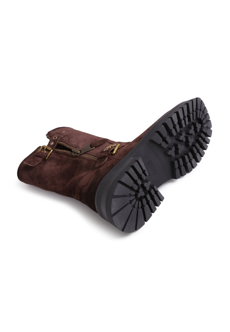 Brauner Wildlederstiefel mit einer schwarzen Gummisohle, ausgestattet mit einem seitlichen Reißverschluss und dekorativen Schnallen. Die Sohle hat ein robustes Profil für besseren Halt.