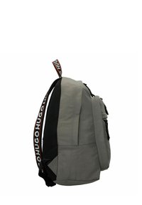 Zaino in tessuto grigio con un pannello laterale nero texturizzato, chiusura con zip e manico superiore con una tracolla con il logo "HUGO".