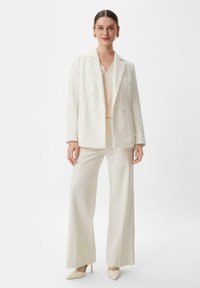 Witte, gestructureerde blazer, crèmekleurige top en wijde broek. Compleet met puntige hakken, wat een monochroom, op maat gemaakt ensemble creëert.