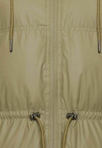 Chaqueta acolchada de tono claro con cremallera frontal, cordones ajustables y acentos metálicos. Textura suave con un acabado ligeramente brillante.