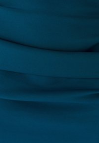 Türkiissinine veniv kangas, millel on õrn voltimine ja sile tekstuur, kus pehmed voldid loovad kihilise välimuse.